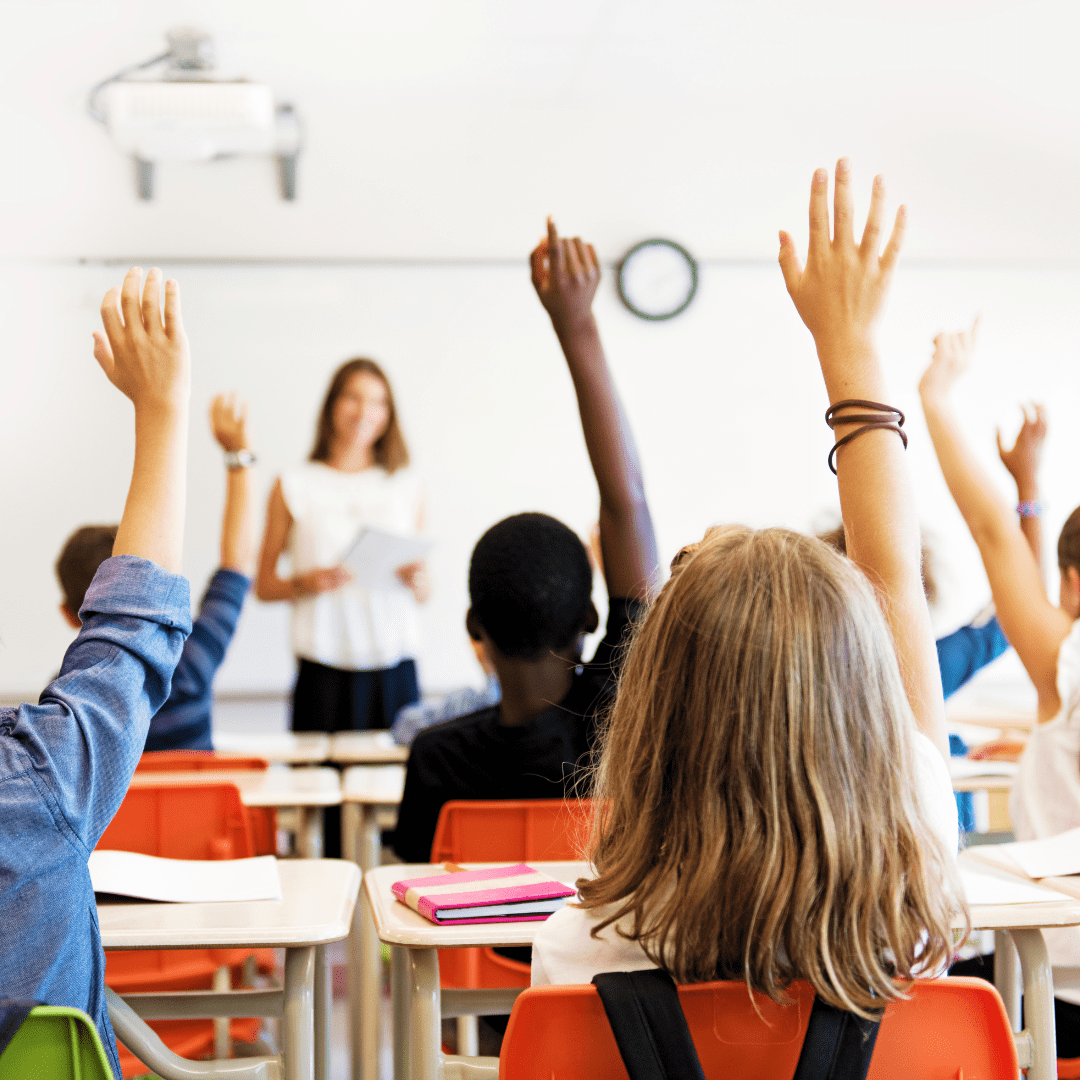 Pupils in a classroom facing the board with their hands raised